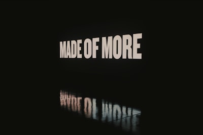 Large bold white letters spelling 'MADE OF MORE' are displayed against a dark background, with the words reflected on a glossy surface below.