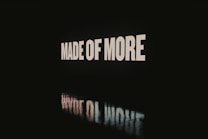 Large bold white letters spelling 'MADE OF MORE' are displayed against a dark background, with the words reflected on a glossy surface below.