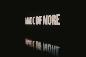 Large bold white letters spelling 'MADE OF MORE' are displayed against a dark background, with the words reflected on a glossy surface below.