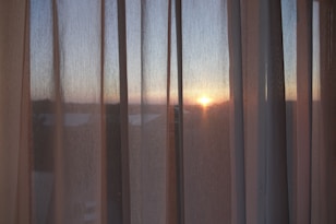 the sun is setting through the sheer curtains