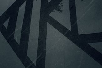 Abstract charcoal and sand-toned geometric shapes casting soft shadows on a dark textured background.