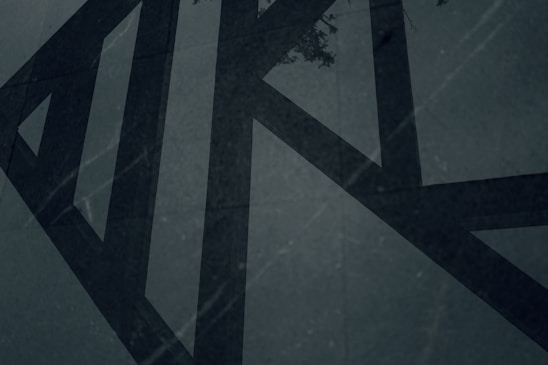 Abstract charcoal and sand-toned geometric shapes casting soft shadows on a dark textured background.