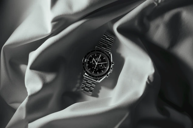 Close-up of a gleaming gold watch resting on a dark velvet cushion with subtle golden light reflections.
