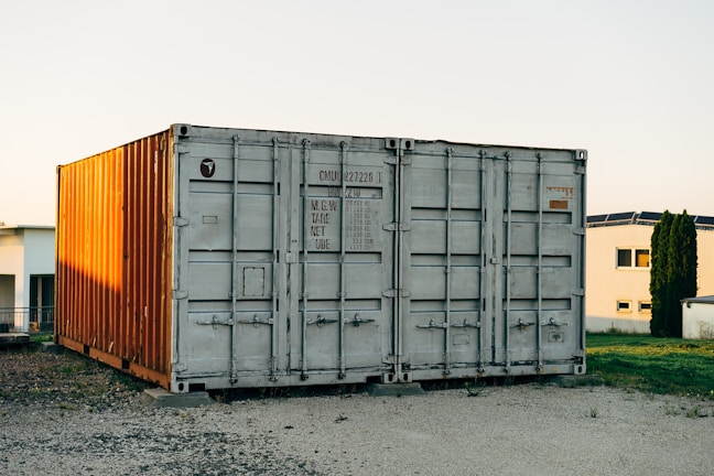 A sleek shipping container home at dusk, illuminated warmly from within against a charcoal sky.