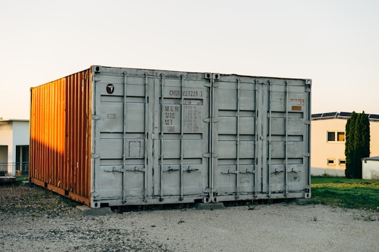 A vibrant photo showing a container home nestled in a green yard with sunlight casting warm shadows.