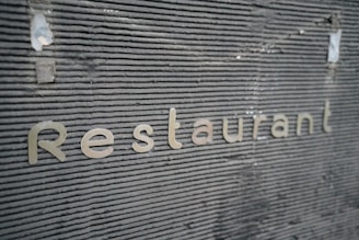 Metallic letters spelling 'Restaurant' are embedded against a textured, dark gray surface. The surface features horizontal grooves giving it a modern, industrial look.