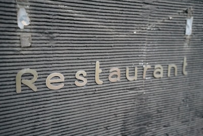 Metallic letters spelling 'Restaurant' are embedded against a textured, dark gray surface. The surface features horizontal grooves giving it a modern, industrial look.
