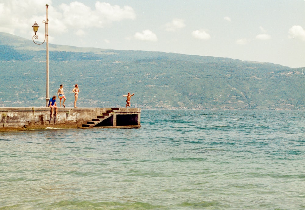 a group of people standing on a pier next to a body of water