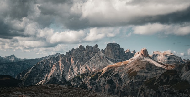 A dynamic shot of a mountain range with dramatic clouds casting shadows over the rugged terrain.