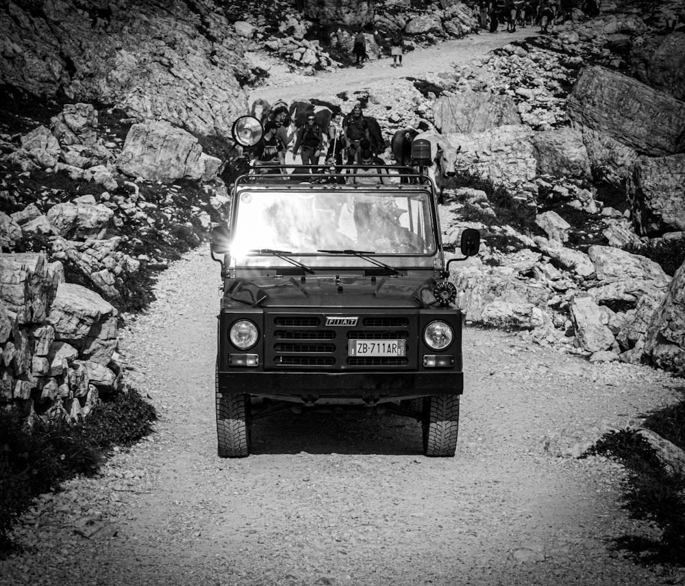 a black and white photo of a jeep driving down a dirt road