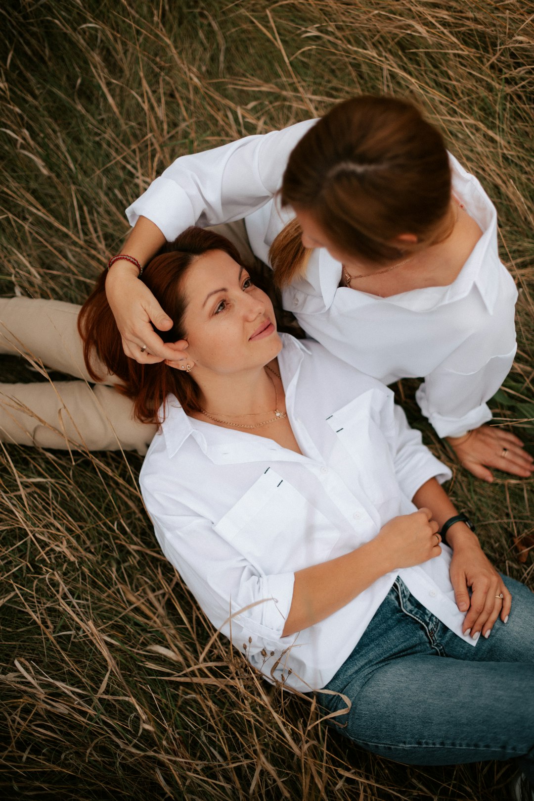 a couple of women sitting on top of a grass covered field