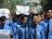 A group of young men wearing blue shirts and black ties are participating in a protest. Some are holding up signs with messages demanding justice and peace. The mood is assertive and determined.
