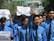 A group of young men wearing blue shirts and black ties are participating in a protest. Some are holding up signs with messages demanding justice and peace. The mood is assertive and determined.