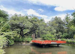 a red bridge over a body of water surrounded by trees