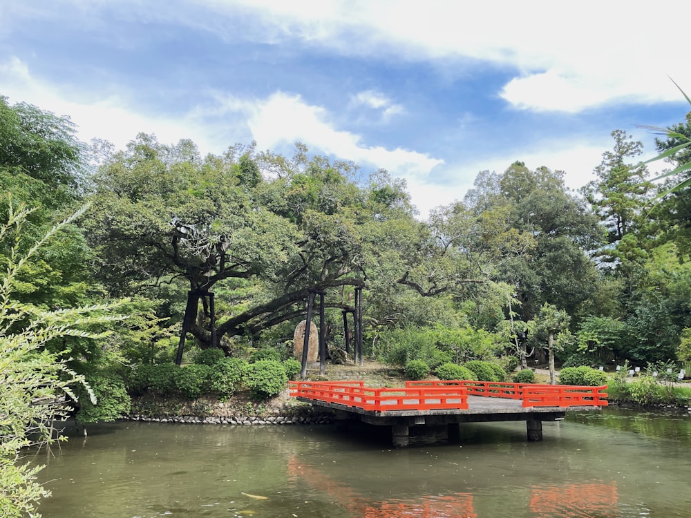 a red bridge over a body of water surrounded by trees