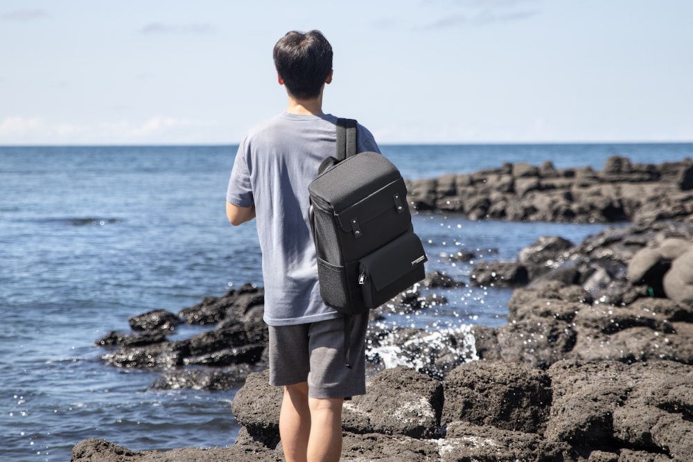 a man with a backpack standing on rocks by the ocean