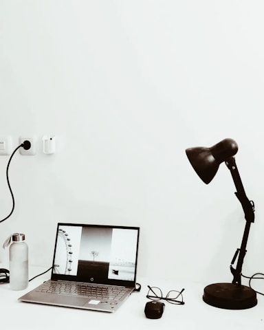 A minimalist workspace with a charcoal grey camera bag and a laptop displaying a photo editing software.