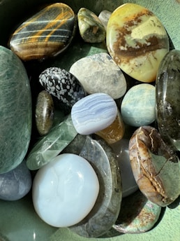 A collection of smooth, polished stones with various colors and patterns. They range from bright white to deep greens, with some exhibiting unique striped or marbled designs. The stones are arranged closely together, creating a harmonious and balanced visual display.