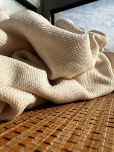 Close-up of soft, textured linen fabric draped over a cozy bed in warm natural light.