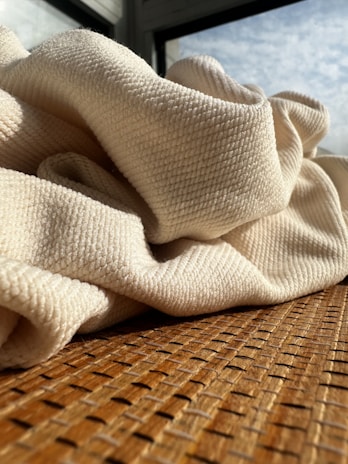 Close-up of soft, textured fabrics in neutral tones layered gently on a chair by natural sunlight.