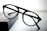 A pair of round black eyeglasses with a thin frame is placed on a dark rectangular object with a soft gradient background. The glasses appear to be stylish and simple, with clear lenses and bold frames.