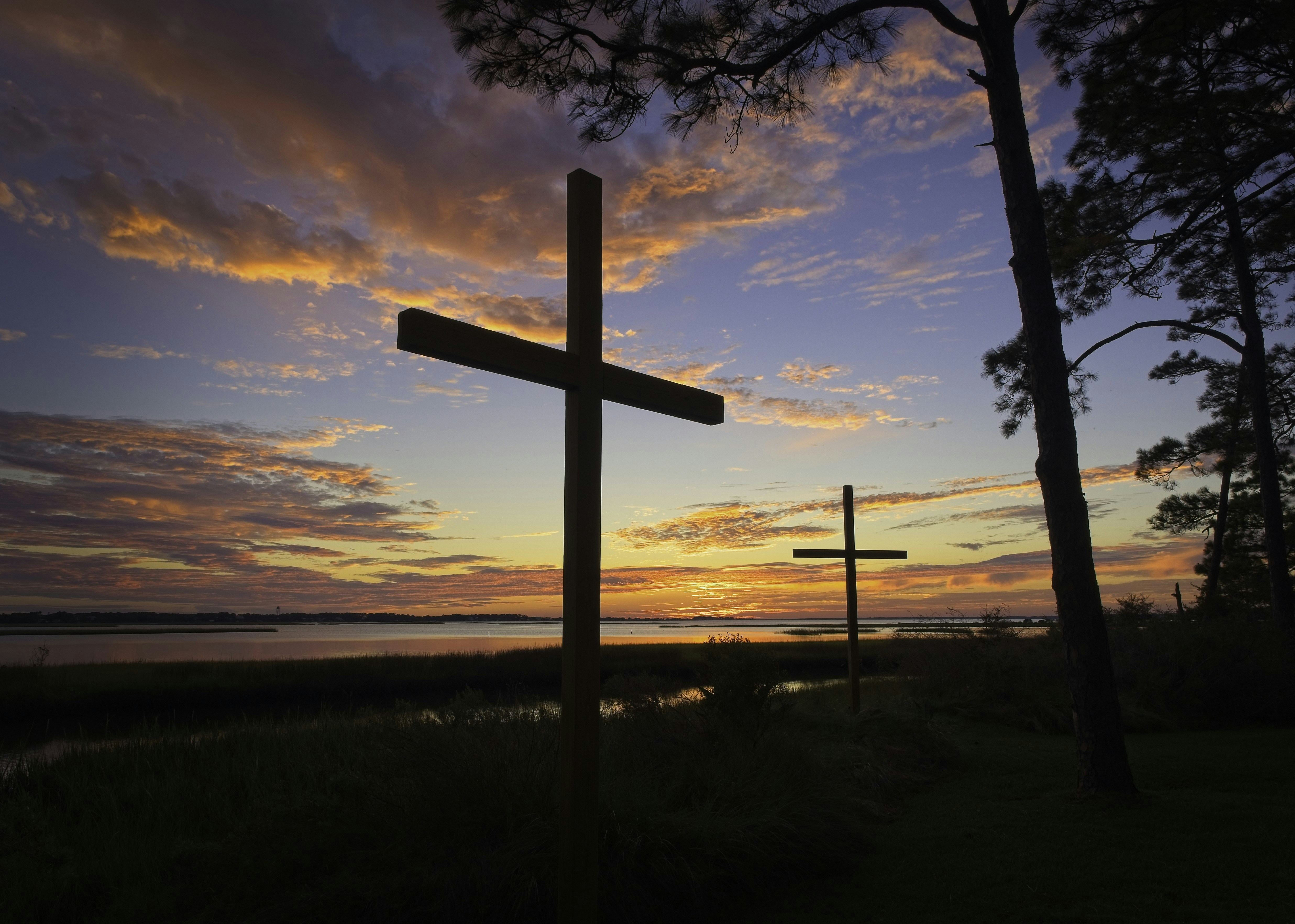 a cross is silhouetted against a sunset over a body of water