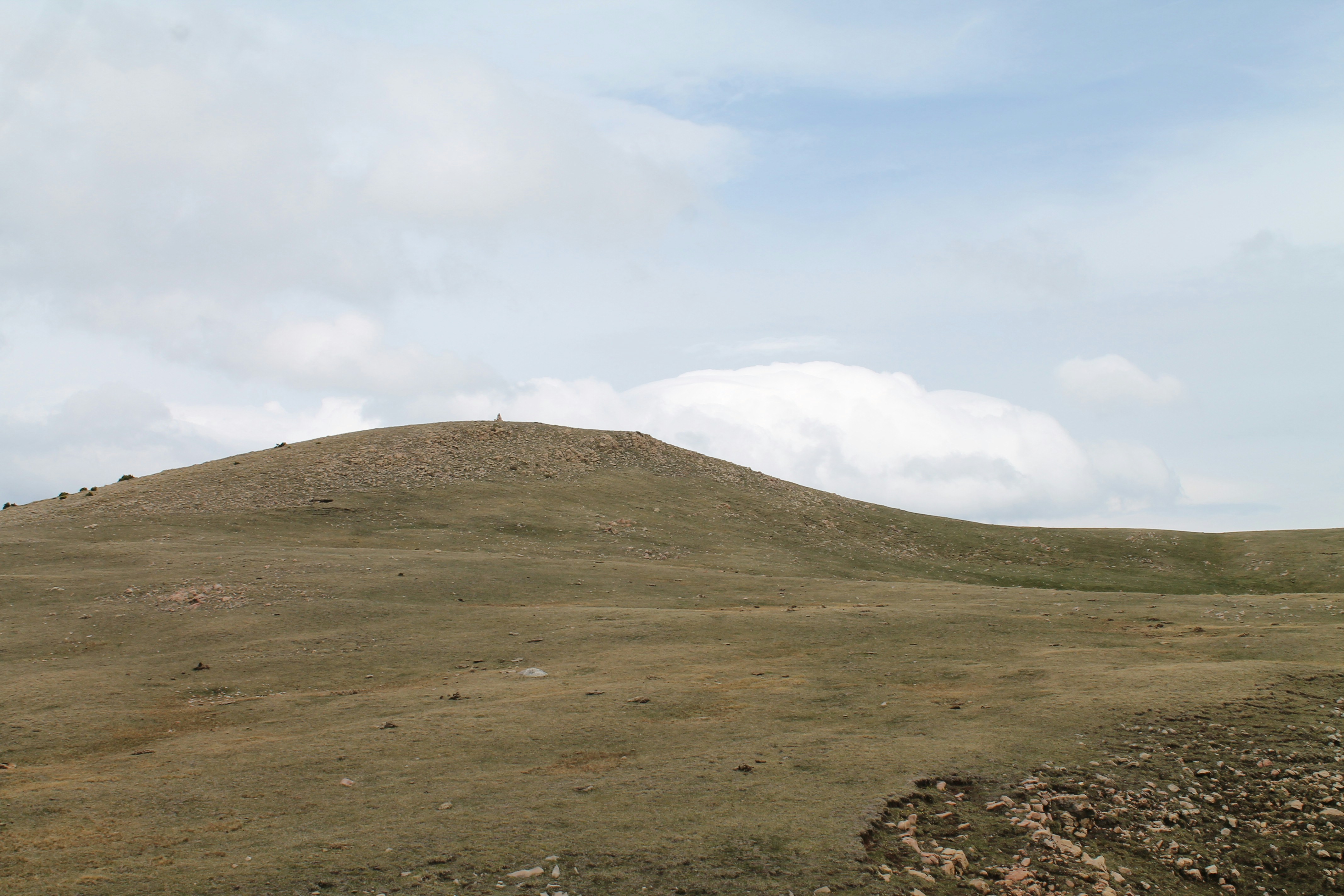 a grassy hill with a few clouds in the sky