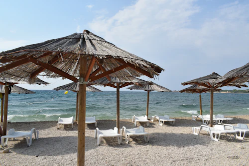Parasols de paille et transats blancs sur une plage de galets, mer agitée