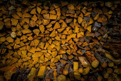 A neatly stacked pile of firewood arranged in a compact manner. The logs are cut into various shapes, primarily circular and semi-circular, showcasing different shades of brown and wood textures. The image is taken in a warmly lit environment that highlights the detailed patterns and grain of the wood.