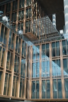 A modern architectural building features a facade with large glass windows and gold-colored metal frames. The design includes overlapping structures and reflective surfaces, creating a sense of depth and modernity.