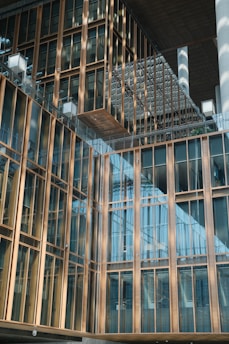 A modern architectural building features a facade with large glass windows and gold-colored metal frames. The design includes overlapping structures and reflective surfaces, creating a sense of depth and modernity.