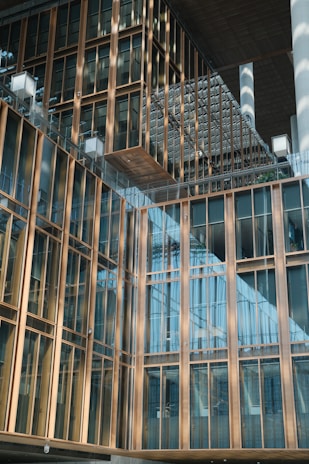 A modern architectural building features a facade with large glass windows and gold-colored metal frames. The design includes overlapping structures and reflective surfaces, creating a sense of depth and modernity.