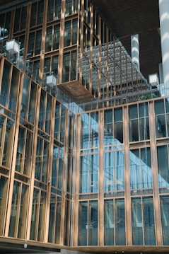 A modern architectural building features a facade with large glass windows and gold-colored metal frames. The design includes overlapping structures and reflective surfaces, creating a sense of depth and modernity.