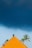 A vibrant orange-tiled roof sits beneath a dramatic dark sky, with a backdrop of tall palm trees swaying gently. The contrast between the bright roof and the ominous clouds creates a striking visual effect.