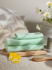 a pile of towels sitting on top of a bed next to a vase of flowers