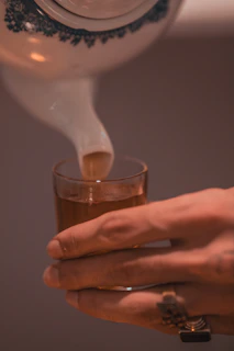 Hands gently pouring hot water over loose herbal tea leaves in a glass teapot