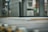 A close-up view of a piece of particle board with two visible holes on its side, placed on a metal conveyor belt within an industrial setting. The background is blurred, highlighting machinery and equipment.
