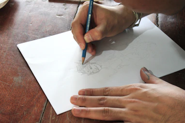 Close-up of hands sketching intricate blueprints on soft parchment paper.