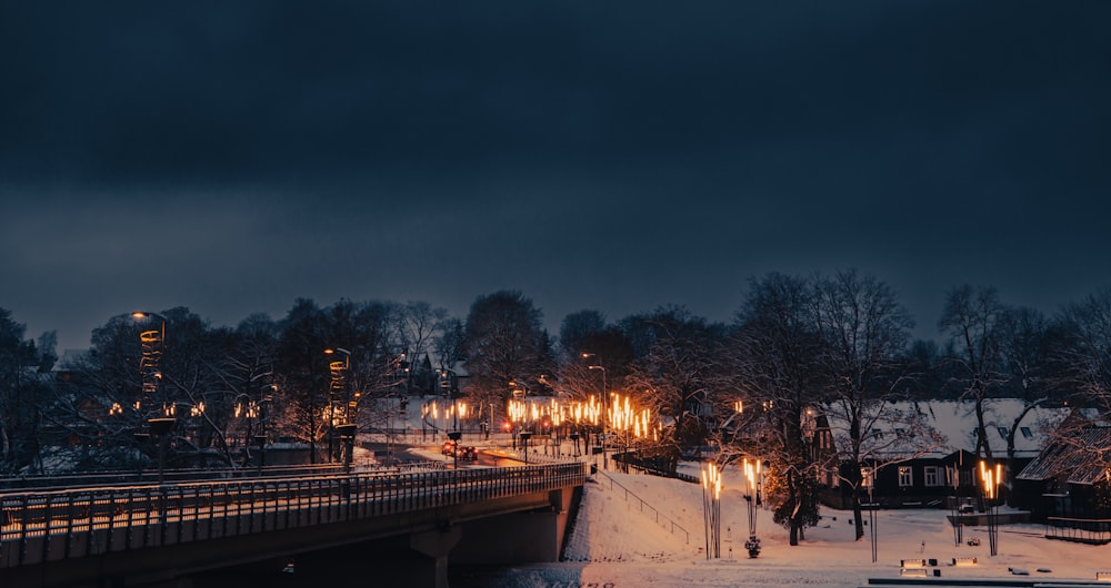 a night scene of a snowy town with a bridge