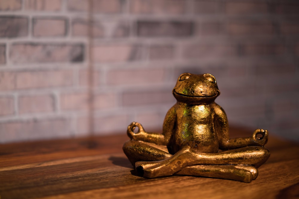 una estatua de rana dorada sentada encima de una mesa de madera