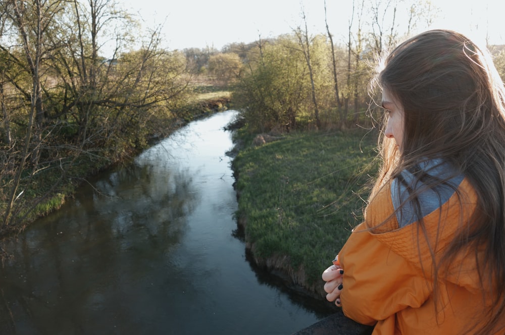 a girl in an orange jacket looking out over a river
