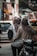 Two people wearing hijabs walk closely together down a bustling urban street. One is carrying a black bag while the other has their arm around the first person. They are surrounded by blurred background elements that suggest a busy market or street scene, with vehicles and colorful objects.