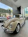 A happy customer standing next to a beautifully restored vintage car in a bright showroom.