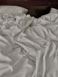 an unmade bed with white sheets and pillows