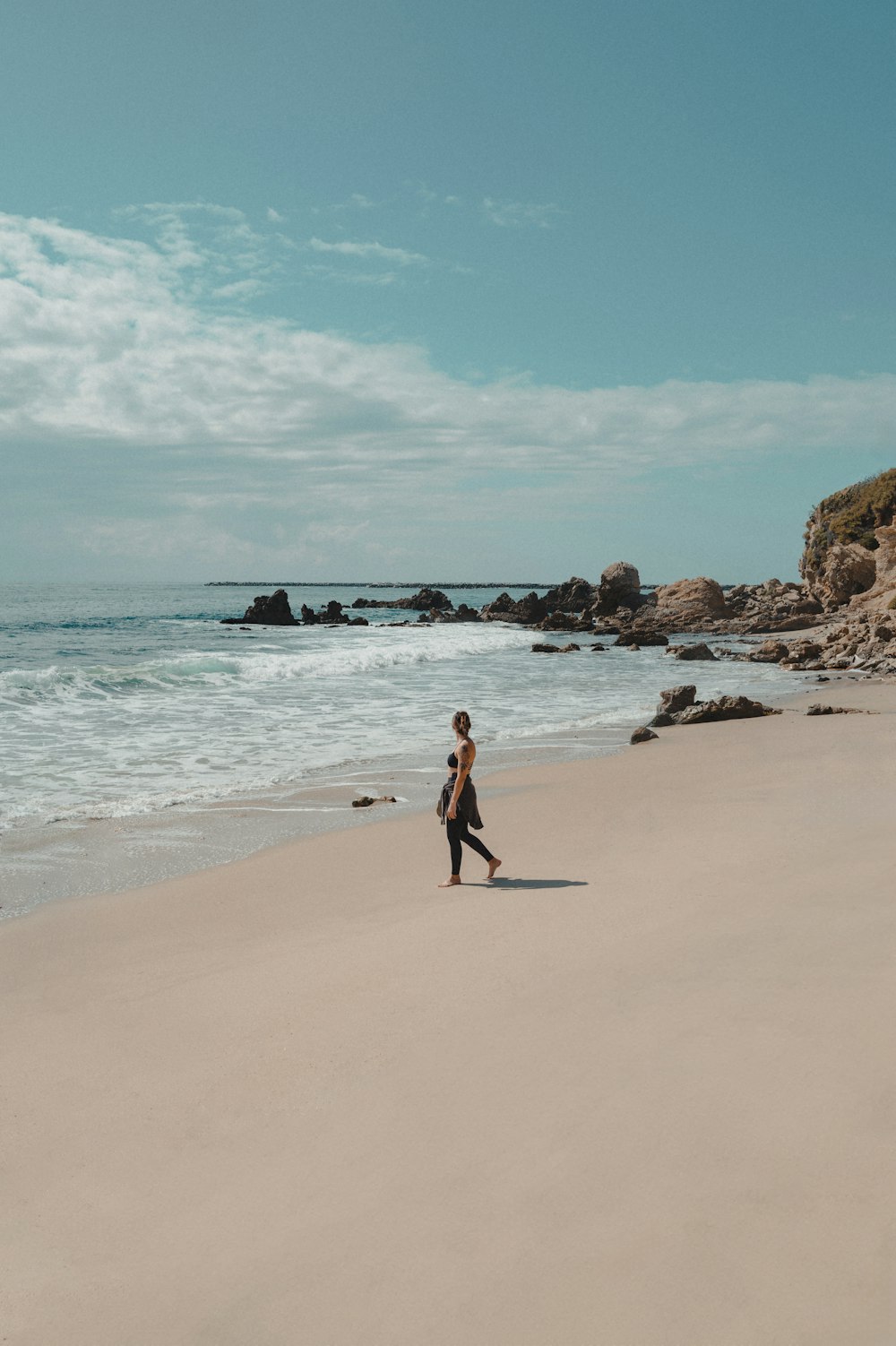 a woman walking along a beach next to the ocean