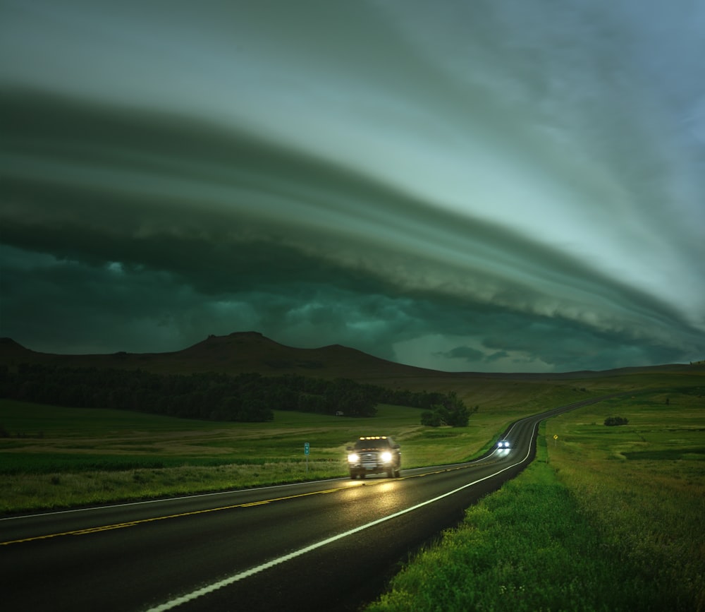 a car driving down a road under a storm cloud