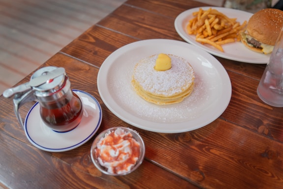 A cozy wooden table set with a stack of fluffy pancakes drizzled in maple syrup and fresh berries, next to a steaming cup of latte.