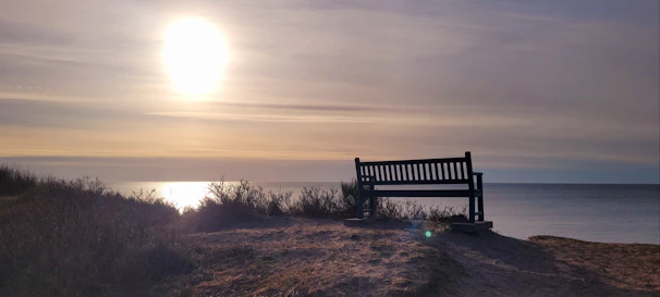A sleek backless bench on a sandy beach patio with soft cushions and ocean waves in the background.