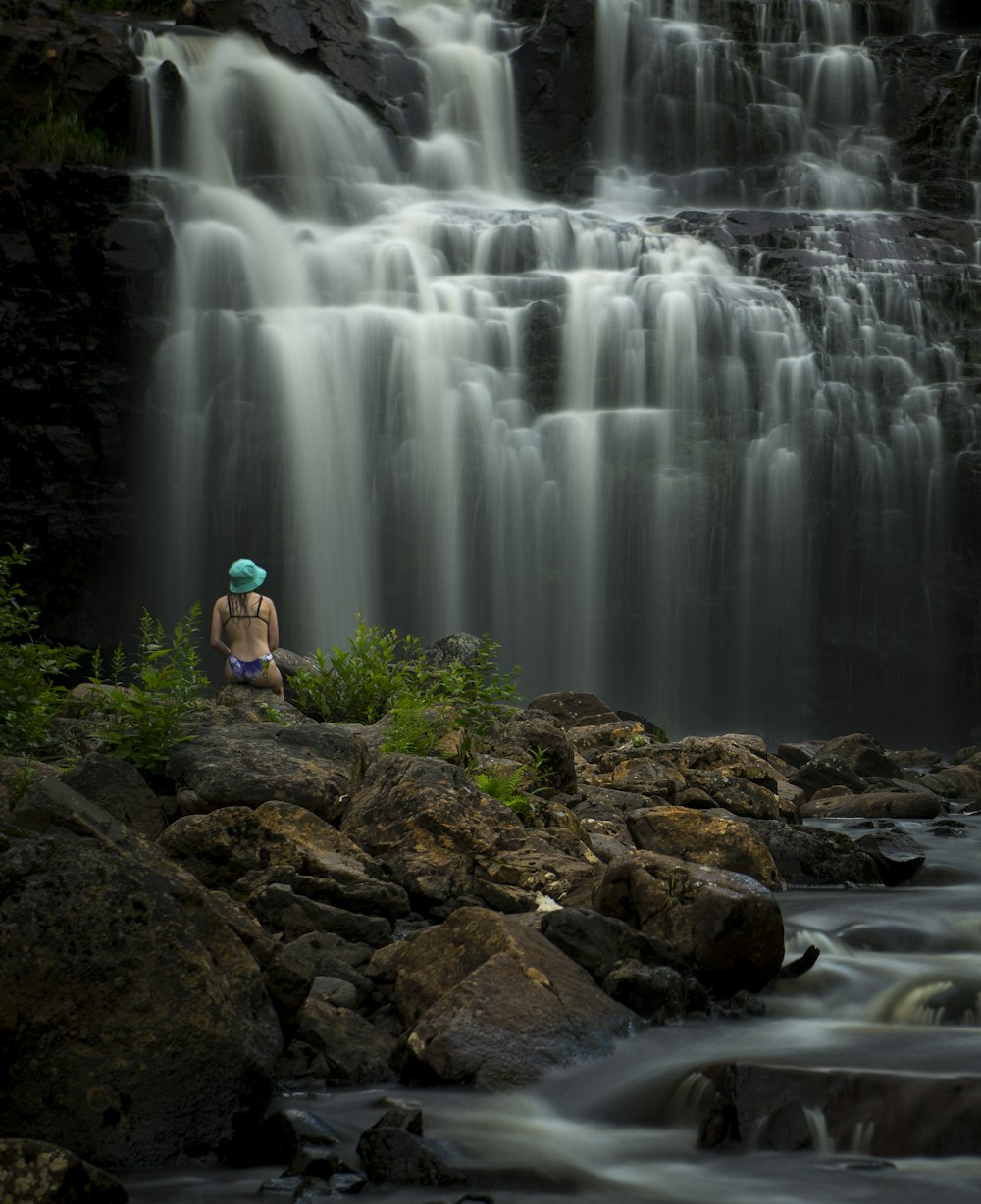 a person sitting on a rock in front of a waterfall