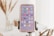 A smartphone is mounted on a tripod, showcasing a variety of app icons on its screen. The background is softly focused, revealing hints of an indoor setting with dried plants and furniture.